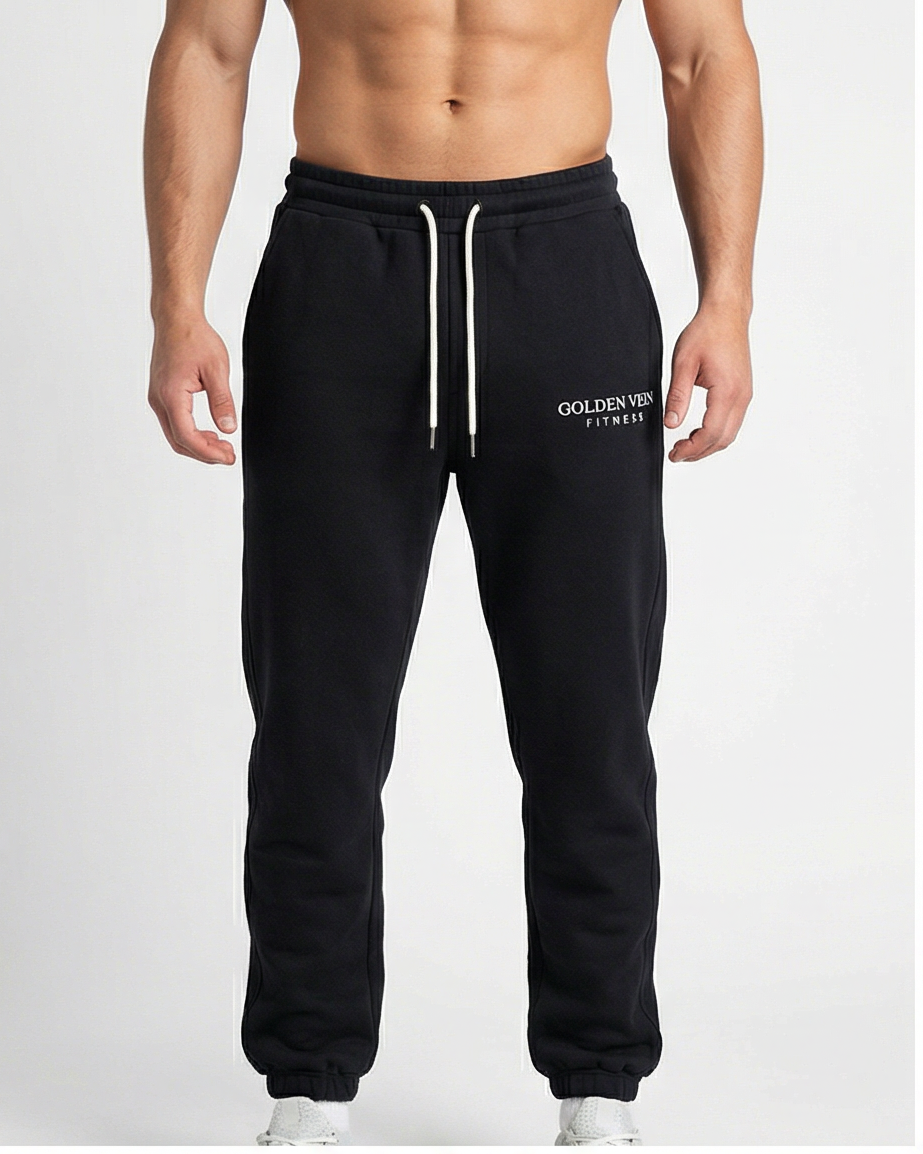 Schwarze GV Essential Sweatpants, frontale Studioaufnahme an einem männlichen Fitness-Model; elastischer Bund, klare Silhouette und weiche Baumwollstruktur.