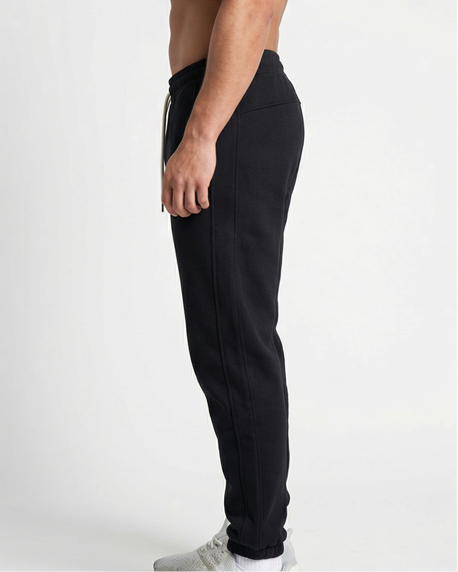 Schwarze GV Essential Sweatpants, seitliche Studioansicht eines männlichen Models; Fokus auf Seitennaht, Beinverlauf und Materialfall.