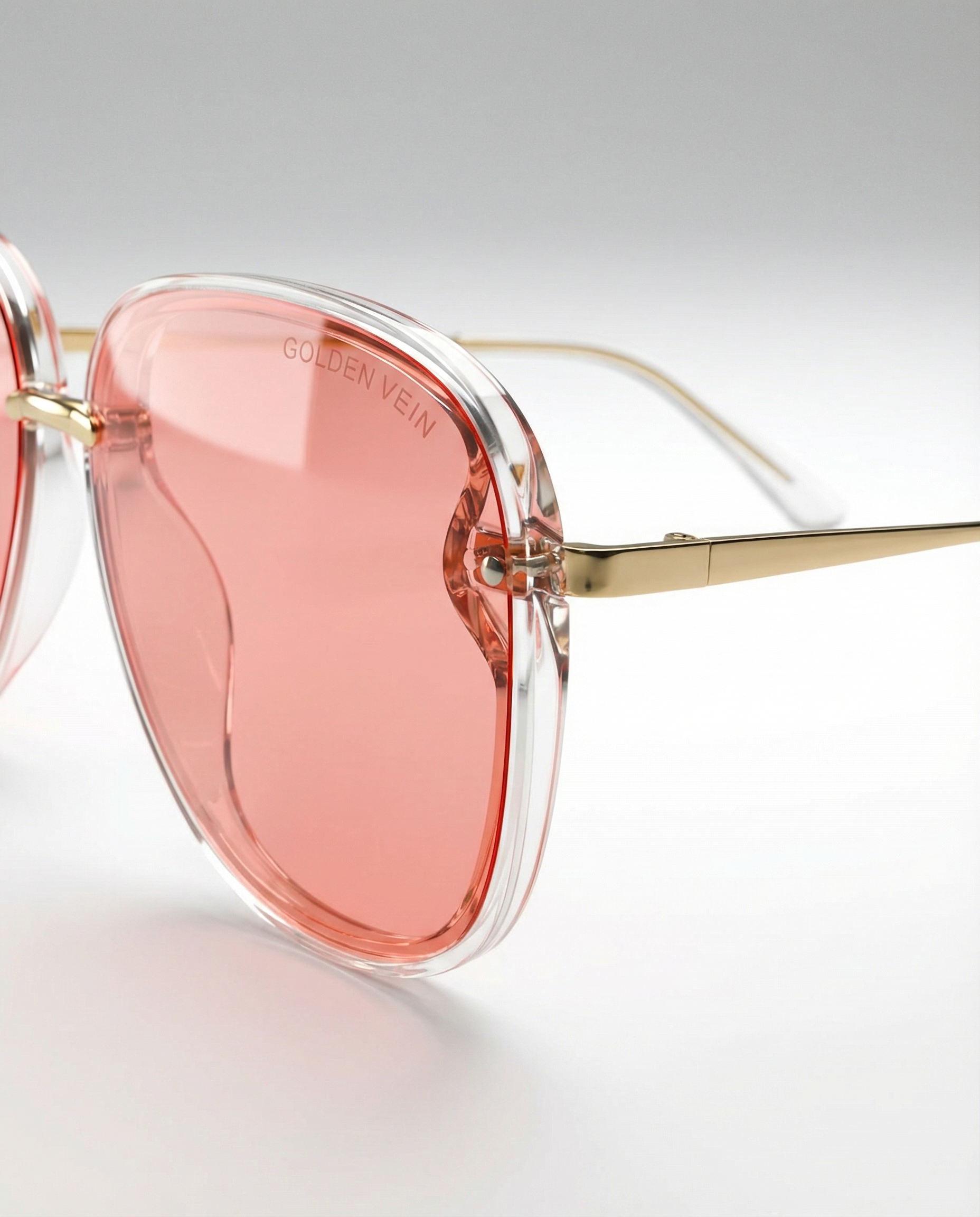 Rosa Golden Vein „Aurelia“ Sonnenbrille mit leicht getönten Gläsern, elegant geschwungenem Rahmen und goldfarbenen Details, fotografiert vor neutralem Studiohintergrund.